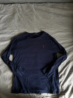 Ralph lauren tröja mörkblå - En mörkblå Ralph lauren tröja i färgen mörkblå med långa armar men tunn som en T-shirt. Perfekt under annat klädesplagg vid kallt väder och funkar lika bra vid varmare temperatur eftersom den är så tunn. Kontakta vid fler frågor. 