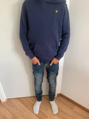 Nudie Jeans - Säljer ett par blå slim fit jeans med snygga slitningar och tvättade detaljer. Saknar knapp, se bild. Jeansen har klassisk femficksdesign och smal passform som sitter tajt längs benen. Storlek W27/L33. Perfekta för en avslappnad och trendig look.