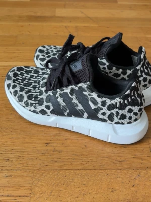 Adidas sneakers med leopardmönster - Snygga Adidas sneakers med svartvitt leopardmönster och klassiska tre ränder på sidan. Ovandelen är i textil med svarta skosnören och vit sula. Perfekta för dig som vill sticka ut med ett djurmönstrat par sneakers.