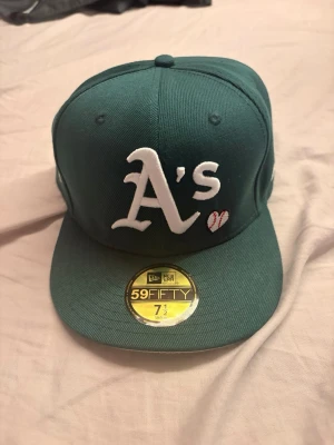 Grön Oakland A's keps 59FIFTY - Snygg grön keps från New Era 59FIFTY med Oakland A's logga broderad framtill och 1989 World Series-märke på sidan. Klassisk flat brim och strukturerad passform. Perfekt för dig som gillar sportig stil och baseball-inspirerade accessoarer.