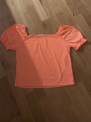 Persikofärgad topp med puffärm - Söt persikofärgad topp med puffiga korta ärmar och fyrkantig ringning. Tillverkad i mjukt bomullsmaterial som känns skönt mot huden. Perfekt för dig som vill ha en färgklick i garderoben och gillar trendiga detaljer.
