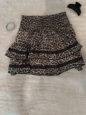 Leopardmönstrad volangkjol från Lindex - Säljer en kort leopardmönstrad kjol från Lindex med bred resår i midjan och dubbla volanglager. Kjolen har svarta spetsdetaljer och är perfekt för dig som vill sticka ut lite extra. Materialet känns lätt och luftigt🎀🫰🏻.