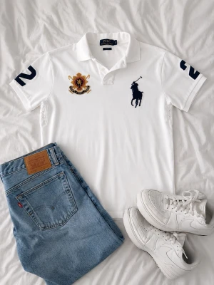 Vit slim fit piké Polo Ralph Lauren - Vit pikétröja från Polo Ralph Lauren i slim fit med klassisk krage, knappar och broderad marinblå logga samt emblem på bröstet. Siffror på ärmarna för sportig vibe. Tillverkad i mjuk bomull.