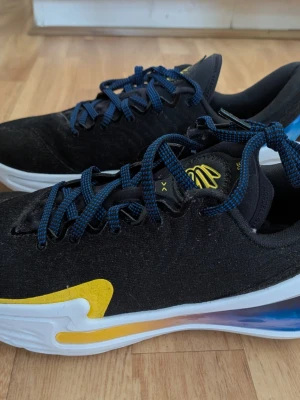 Helt nya Under Armour sneakers - Snygga svarta Under Armour sneakers med blå snören och vita sulor. Skorna har gula detaljer på sidan och logga på plösen. Ovandelen är i textilmaterial och sulan är tjock för extra komfort. Perfekta för dig som gillar sportig stil. Storlek 42.5. Ingen skokartong.