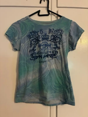 Blågrön t-shirt med tryck - Cool t-shirt i blågröna nyanser med unikt mönster och tryck framtill och baktill. T-shirten har korta ärmar. Perfekt för dig som gillar streetstyle och grafiska detaljer.