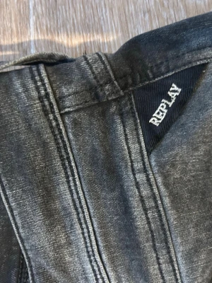 Svarta Replay jeans med tvättad look - Säljer ett par svarta jeans från Replay med tvättad, lite sliten look. Klassisk femficksmodell med Replay-logga på bakfickan och detaljer i silver. Jeansen har raka ben och är tillverkade i mjuk denim.