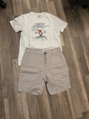 Beige bomullsshorts med knapp - Snygga beige shorts i bomull med klassisk passform och knappstängning fram. Shortsen har bälteshällor, två sidofickor och två bakfickor med knappdetalj. Perfekta för varma dagar och enkel att matcha med olika stilar. Med en Nike t-shirt och basket 