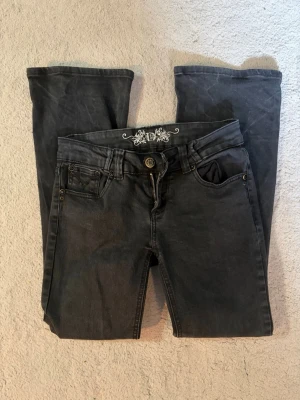 Svarta bootcut jeans med broderi - Snygga svarta jeans med bootcut  och dekorativa broderier på bakfickorna. Klassisk femficksmodell med metallknappar och nitar. Jeansen har normal midja och är tillverkade i ett mjukt denimtyg som ger en avslappnad look.
