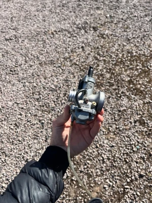 Polini förgasare 21mm - Säljer en metallfärgad förgasare med slang, perfekt för dig som vill trimma eller byta ut din nuvarande del på moped eller motorcykel. Kompakt design med tydliga justerskruvar och anslutningar. Passar flera olika modeller.