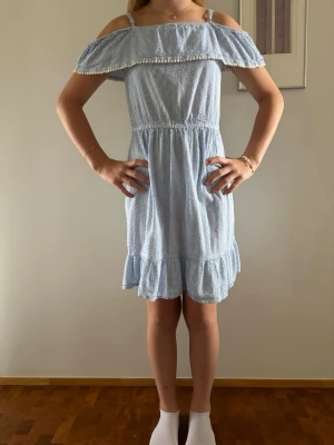 2 offshoulder klänningar, en gul och en blåvit randig - Söta kortklännigar som är blåvit randig och gul med offshoulder och smala axelband. Klänningarna har volangkant upptill och nertill samt resår i midjan för en bekväm passform. Perfekt för varma dagar och har en lätt, luftig känsla.