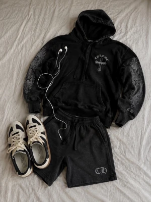 Svart hoodie med tryck från Chrome Hearts - Svart hoodie från Chrome Hearts med stora vita tryck på ryggen och ärmarna, samt ett mindre tryck på bröstet. Hoodien har huva, magficka och ribbade muddar. Storlek S.