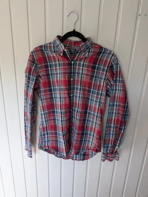 Rutig skjorta från Polo Ralph Lauren - Klassisk rutig skjorta från Polo Ralph Lauren i slim fit. Skjortan har långa ärmar, knappar framtill och en snygg mix av rött, blått och vitt. Perfekt för dig som gillar en tidlös och avslappnad stil.