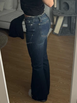 Mörkblå bootcut jeans med fransig midja - Säljer ett par mörkblå bootcut jeans med fransig midja. Jeansen är lågmidjade och lätt slitna detaljer nertill. Ordinarie pris - 599kr