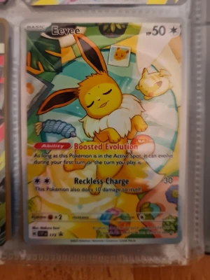 Pokémonkort Eevee Boosted Evolution - Säljer ett färgglatt Pokémonkort med Eevee-motiv. Kortet har en lekfull design med Eevee som vilar bland leksaker och har förmågan Boosted Evolution samt attacken Reckless Charge. Bakgrunden är gul, blå och grön med detaljerade illustrationer.
