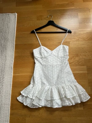  Ny populärt Vit kort klänning med volang - Söt vit kort klänning med tunna axelband och volangkant. Klänningen har ett broderat hålmönster och omlottinspirerad byst. Perfekt för varma dagar och sommarens alla tillfällen.