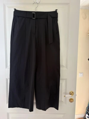 Svarta vida kostymbyxor med bälte - Snygga svarta kostymbyxor med hög midja och tillhörande bälte i samma tyg. Byxorna har vida ben och pressveck framtill för en clean look. Perfekta för dig som gillar en stilren och modern outfit. Kolla gärna mina andra annonser❗️