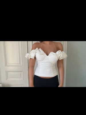 Vit offshoulder korsettopp - Supersnygg vit korsettopp med offshoulder och puffiga ärmar. Toppen har en figurnära passform och markerad byst, vilket ger en elegant siluett. Skriv vid frågor!!