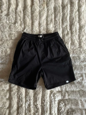 Svarta Les Deux-shorts i storlek 30 - Sköna casual Les Deux shorts i mjuk bomull (97% bomull, 3% elastan) så de har lite stretch. Elastisk midja med knytsnöre, sidofickor och en bakficka – enkel svart modell som matchar allt nu till sommaren.  Använd men i mycket fint skick, inga hål eller fläckar.  Rök- och djurfritt hem. Skriv gärna om du vill ha fler bilder eller undrar något!