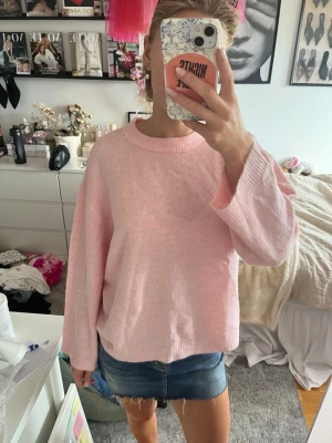 Ljusrosa oversized stickad tröja - Mysig ljusrosa stickad tröja med oversized passform och rund hals. Tröjan har långa ärmar och ribbade muddar vid ärmslut och nederkant. Perfekt för dig som gillar en avslappnad och trendig stil.