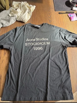 Svart Acne Studios t-shirt - Snygg svart t-shirt från Acne Studios med tryck 'STOCKHOLM 1996' på bröstet. Klassisk passform och rund halsringning. Perfekt till jeans eller shorts för en clean och stilren look.