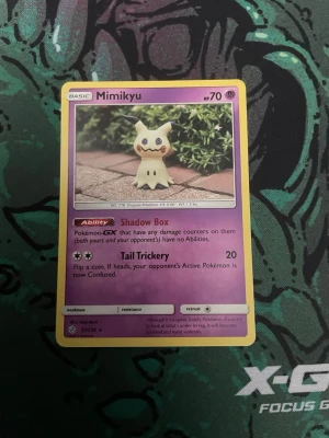 Pokémonkort Mimikyu - Säljer ett Pokémonkort med Mimikyu-motiv. Kortet har lila ram och detaljer, samt visar Mimikyu med förmågan Shadow Box och attacken Tail Trickery. Perfekt för samlare eller Pokémonfans som vill utöka sin kortsamling.