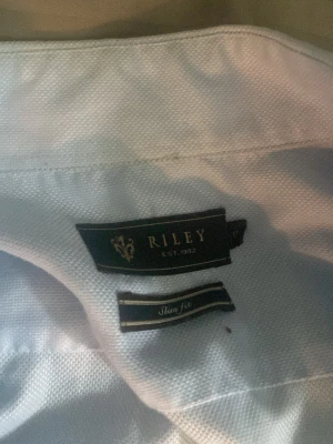 Ljusblå skjorta från Riley - Säljer en stilren ljusblå skjorta från Riley med klassisk krage och knappar framtill. Skjortan har lång ärm och är i slim fit-modell, vilket ger en snygg och modern passform. Perfekt till både jeans och chinos.