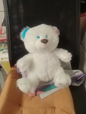 Vit mjuk nallebjörn med färgglada öron - Söt vit nallebjörn i mjukt plyschmaterial. Ena örat är blått och det andra rosa, med blå ögon och brunt nosparti. Perfekt som present eller mysig inredningsdetalj i sovrummet.