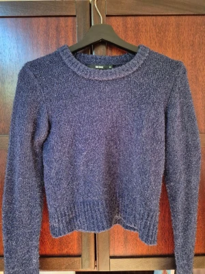 Blå stickad tröja med skimmer - En stickad mörkblå tröja med rund krage och långa ärmar. Perfekt till jeans och kjol. Kort i modellen, skimrande i ljus. 