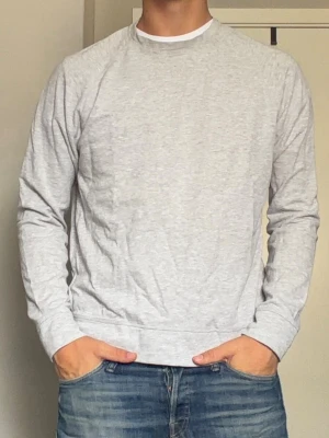 Ljusgrå basic sweatshirt - En stilren ljusgrå sweatshirt med rund hals och långa ärmar. Tröjan har en klassisk passform och är tillverkad i mjukt bomullsmaterial. Perfekt för en avslappnad look och enkel att matcha med jeans eller andra byxor.