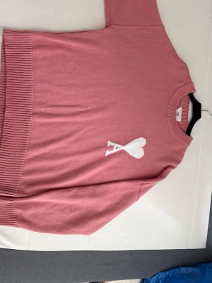 Rosa stickad tröja med hjärtdetalj från Ami paris - Säljer en rosa stickad Ami paris tröja med vit hjärtdetalj och bokstaven A på bröstet. Tröjan har rund hals, ribbade muddar och är tillverkad i mjukt material. Perfekt för dig som gillar en söt och trendig look. Pris kan diskuteras