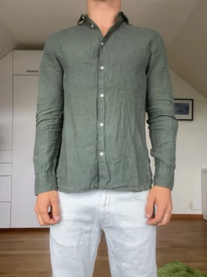 Grön linneskjorta från Riley - Olivgrön skjorta från Riley tillverkad i 100% linne. Strl S. Inga defekter. Modellen är 178 cm och väger 77 kg. Hör gärna av dig vid frågor!