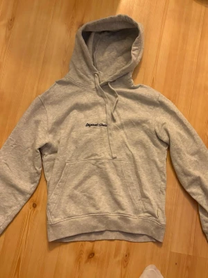 Ljusgrå hoodie från Jack & Jones - Ljusgrå hoodie från Jack & Jones med broderad text 'Originals Studio' på bröstet. Klassisk känguruficka framtill, justerbar dragsko i huvan och mjukt material. Perfekt för en avslappnad och stilren look. Nypris 499kr mitt pris 179