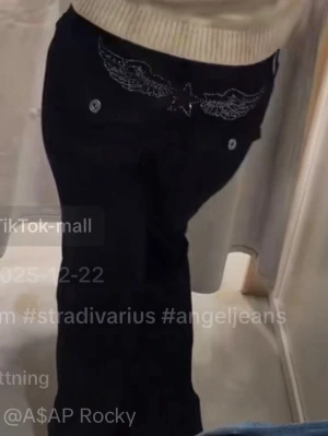 Svarta jeans med änglavingar bak - Säljer ett par svarta lågmidjade jeans med bootcut och snygga broderade diamant änglavingar och stjärna på bakfickorna. Jeansen har två fickor bak med knappdetaljer och är tillverkade i ett klassiskt denimtyg. Perfekta för dig som vill sticka ut med coola detaljer. Helt slutsålda! Storlek L men passar även M