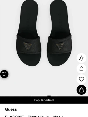 Svarta slip-in sandaler från Guess - Stilrena svarta slip-in sandaler från Guess med bred rem och ikonisk trekantslogga i metall framtill. Sandalerna har platt sula och är tillverkade i syntetmaterial med diskret mönster på remmen. Perfekta för en avslappnad och trendig look.