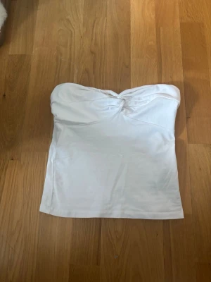 Vit bandeau tubtopp från Gina Tricot - Säljer en vit bandeau tubtopp från Gina Tricot. Toppen är axelbandslös med en snygg rynkning framtill och har en enkel, stilren design. Perfekt att matcha med jeans eller kjol för en fräsch look.