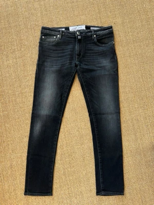 Jacob Cohen Svarta - Snygga svarta skinny jeans från Jacob Cohen med diskreta slitningar och klassisk femficksmodell. Jeansen har en smal passform och är tillverkade i stretchigt denimtyg för extra komfort. Perfekta för en trendig och avslappnad stil.