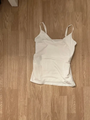 Vit linnetopp med tunna axelband - En enkel och stilren vit linnetopp med tunna axelband. Perfekt att matcha med jeans eller kjol för en clean look. Tillverkad i mjuk bomull som känns skön mot huden. Passar perfekt till sommaren!