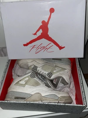 Vita Air Jordan 4 Retro sneakers - Säljer ett par vita Air Jordan 4 Retro sneakers med grå och ljusbeige detaljer. Skorna har meshpaneler, synliga snörhål i plast och den klassiska Jumpman-loggan i rött på plösen. Sulan är tjock och har grå inslag. Kommer i originalkartong.