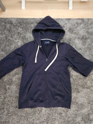 Mörkblå zip hoodie med huva - Snygg mörkblå hoodie från Brandit med dragkedja framtill och stora fickor. Hoodien har beige snören i huvan, Storlek S