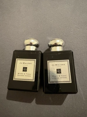 Jo Malone Myrrh & Tonka Cologne Intense - Två flaskor Jo Malone Myrrh & Tonka Cologne Intense. Flaskorna är svarta med silverfärgade, runda lock och har en elegant, rektangulär form. Etiketterna är ljusa med svart text och logga. Doften är känd för sina varma, träiga och kryddiga toner. En för 800 två för 1500kr