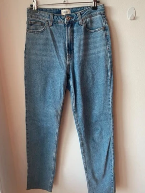 Blå raka jeans från ONLY - Säljer ett par klassiska blå jeans från ONLY med rak passform och hög midja. Jeansen har fem fickor, bälteshällor och stängs med knapp och dragkedja. Tillverkade i denim med en snygg tvättad look. Storleken är Waist 27, Length 34