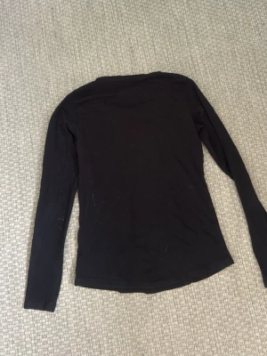 Svart långärmad topp - En svart långärmad topp med rund halsringning och figurnära passform. Tillverkad i mjukt bomullsmaterial som är bekvämt att bära. Perfekt som basplagg och enkel att styla till olika looks.