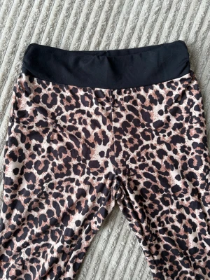 Leopardmönstrade leggings med svart linning - Snygga leggings med leopardmönster i brunt, beige och svart. De har en bred, svart midjeresår som ger en bekväm passform. Perfekta för dig som vill sticka ut med ett djurmönster och samtidigt ha något riktigt bekvämt.
