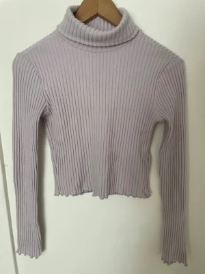 Ljuslila ribbad polotröja crop - Ljuslila stickad polotröja med ribbad struktur och croppad passform. Tröjan har långa ärmar och hög polokrage💜