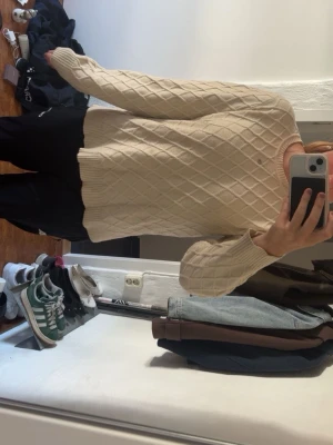 Beige stickad tröja från b.young - Säljer en beige stickad tröja från b.young med ett snyggt rutmönster. Tröjan har rund halsringning, långa ärmar och ribbade muddar vid ärmslut och nederkant. Perfekt för dig som gillar en enkel men stilren look.
