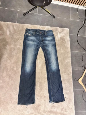 Blå slitna diesel zatiny bootcut jeans. - Ett par blå jeans med raka ben och slitna detaljer, inklusive hål på ena benet och fransiga benslut. Jeansen har klassisk femficksdesign och ljusare tvättade partier framtill. Perfekta för en avslappnad och trendig look. Märket är diesel och modellen är zatiny. W31 L34, priset ej hugget i sten.