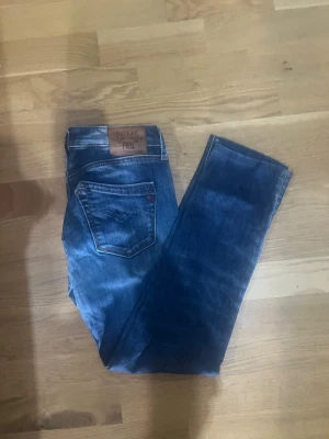 Replay jeans  - Säljer ett par Replay jeans klassiska blå jeans med raka ben och femficksmodell. Jeansen har en snygg läderpatch bak i midjan och subtila slitningar för en avslappnad look. Tillverkade i denim, perfekta till vardagsstilen.