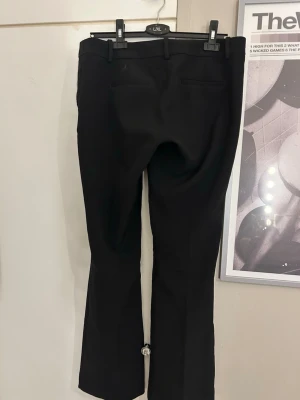 Svarta kostymbyxor med flare/bootcut ben - Snygga svarta. Byxorna har bälteshällor, två fickor bak och är tillverkade i ett mjukt, vävt material som ger en clean look. Perfekta för dig som vill ha en stilren och modern outfit.