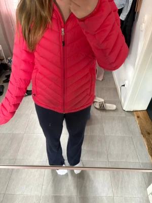 Rosa dunjacka med huva - Snygg rosa dunjacka med huva och dragkedja framtill. Jackan har ett quiltat mönster i chevron-stil och justerbar nederkant. Perfekt för kalla vinterdagar och riktigt lätt att bära. Fodret är grått och jackan har två sidofickor med dragkedja. Den är lite coral i färgen💓 Priset kan diskuteras💓💓