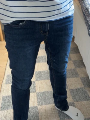 Levis 512 slim jeans mörkblå  - Säljer ett par Levi’s 512 Slim jeans i mörkblå denim, modell “Slim Taper”. Storlek 16A, motsvarar ungefär Small/W28-29. Bra skick utan hål eller fläckar, fint slitage i tvätten. Klassisk 5-fickors modell med kontrastsömmar i orange/gult och äkta Levi’s läderlapp på baksidan.  Perfekta för vardagsbruk – smal passform utan att vara alltför åtsittande.